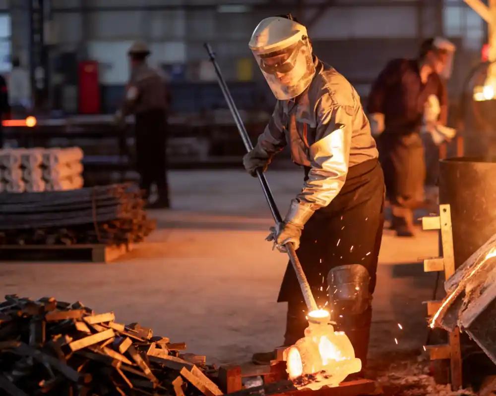 Worker performing metal casting process with molten metal pouring