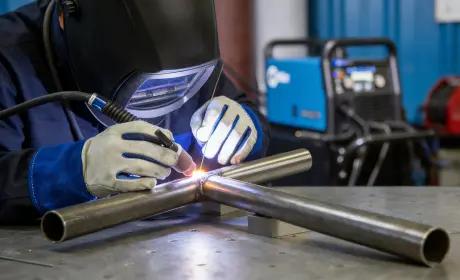 TIG welding on intersecting metal pipes with welder in protective gear
