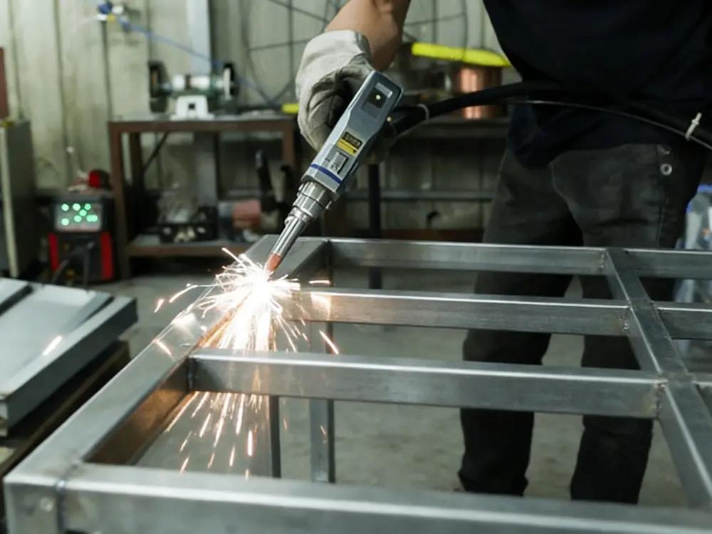 Welding technician using a handheld process on a metal frame with sparks at the weld joint